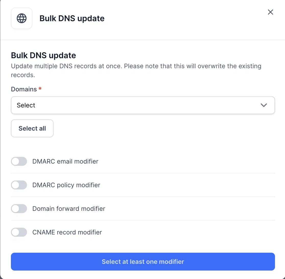 Bulk DNS update dialog with a required Domains dropdown, Select all button, four modifier toggles, and a bottom button requiring at least one modifier. Visible: Bulk DNS update, Update multiple DNS records at once. Please note that this will overwrite the existing records., Domains, Select, Select a