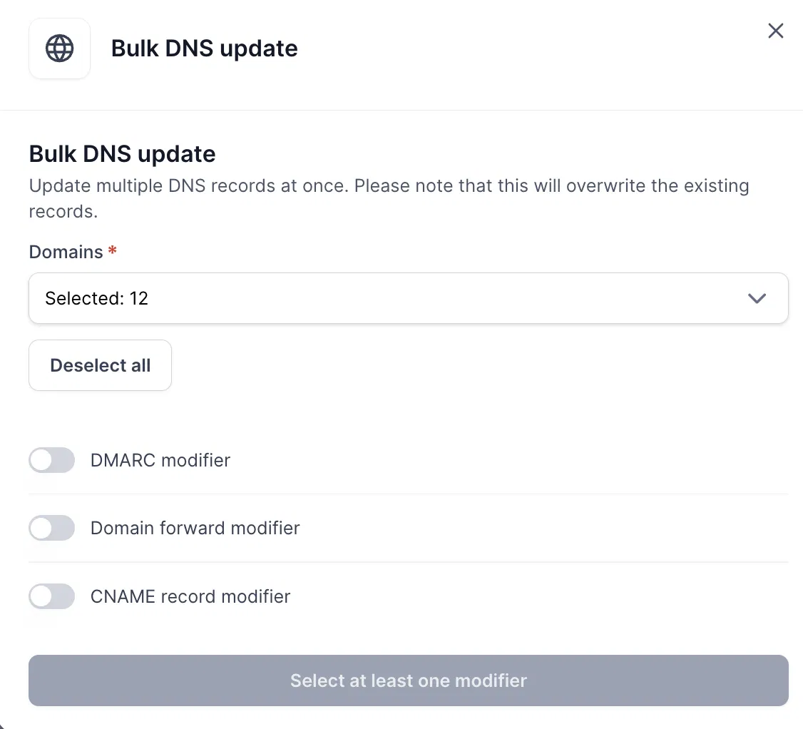 Bulk DNS update form with 12 domains selected, three modifier toggles off, and a disabled button prompting selection of at least one modifier. Visible: Bulk DNS update, Update multiple DNS records at once. Please note that this will overwrite the existing records., Domains *, Selected: 12, Deselect